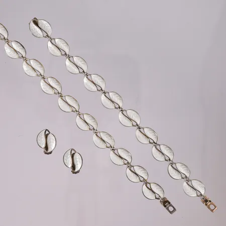 Sett fra David-Andersen i forgylt sølv (halskjede, armbånd og ørepynt med klips), "Dobbel bladranke med hvit emalje" av Willy Winnæs for David-Andersen, 1950-tallet, Lengde kjede 39 cm, Lengde armbånd 17 cm. Hvert dobbelbladet ledd er ca. 18x14mm, 925S Vekt: 45,3 g Kontakt Lånekontoret for frakt