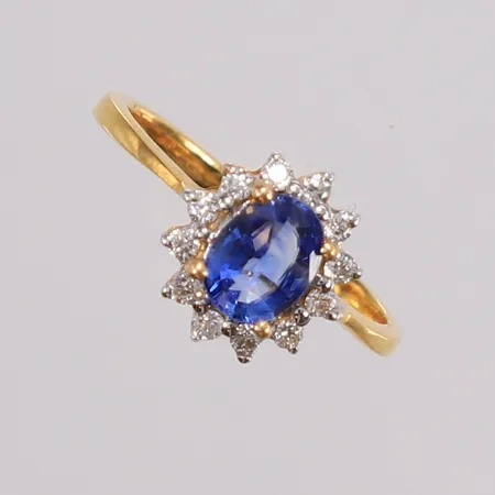 Ring med blå safir og 12 diamanter, ø=16,5 mm, bredde på krone 10x10,8 mm, 18K. Vekt: 2,6 g Kontakt Lånekontoret for frakt