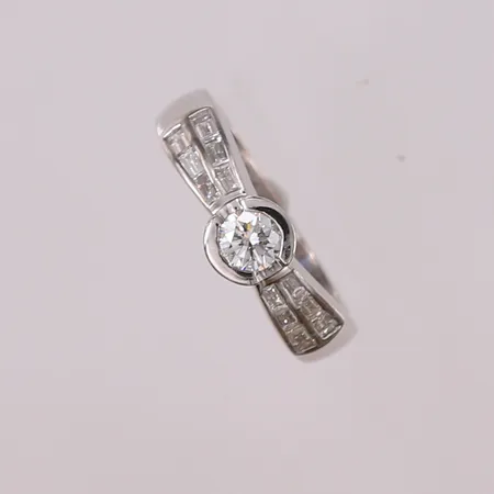 Ring med diamanter (1 x briljantslipt ca. 0,50ct + 12 x baguetteslipte á ca. 0,05ct), ø18,6mm, bredde 3,6- 6,8mm, hvitt gull, 18K Vekt: 7,6 g Kontakt Lånekontoret for frakt