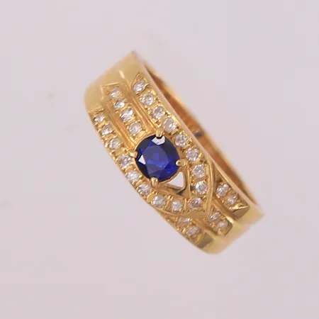 Ring med 27 diamanter (totalt 0,18ct iht. gravering) og blå safir (0,33ct iht. gravering), ø16,2mm, bredde 3,5- 6,8mm, 18K Vekt: 4,3 g Kontakt Lånekontoret for frakt