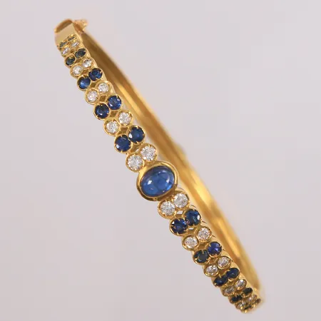 Armring med 20 diamanter ca 0,64ct og 21 safirer, ø 50mm, bredde 3,6 - 7,1mm, 18K Vekt: 16,6 g Kontakt Lånekontoret for frakt