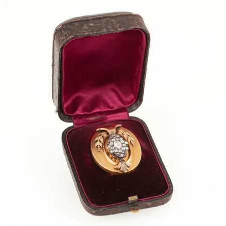 Äldre brosch i 18K guld med 23 rosenslipade diamanter; fattade i silver; med vad som verkar vara originalask. Den är 40,8 x 32,8 mm och väger 13,6g. De runda diamanterna är 2 - 3 mm och den större i mitten är 6,8 x 5,2 mm. Inga stämplar- de har förmodligen suttit på den berlockögla/ -fäste som nu är borttagen. Svensk importstämpel på kroken där nålen fästs. Små ojämnheter.