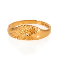 Delvis vildmarksmönstrad ring i 18K guld med en diamant c:a 0,01ct. Den är 1,8 - 7,1 mm bred, är i storlek 17¼ och väger 2,4g. Tillverkad 1989 av Bengt Hallbergs Guldsmeds AB i Köping. Kattfot.