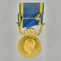 Förtjänstmedalj Gustaf VI Adolf, 23K guld med bandfäste i 18K, Ø27 mm, namngravyr, viktfördelning 23K ca 10g, fäste 18K ca 3,8g.