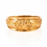 Kupad, kraftig ring i 18K guld med blomstermönster. Den är 5 - 10,3 mm bred, är i storlek 21¾ och väger 8,7g. Tillverkad 2008 av Bengt Hallberg Guldsmeds AB. 