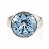 Ring i silver med en blå sten i hög fattning. Den är 4,4 - 14,2 mm bred, är i storlek 16½ och väger 9,7g. Tillverkad 1967 av J Petterssons Eftr Juvelerar AB i Stockholm. Kattfot. 