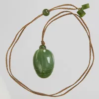 Amulett, snidad jade, 37x23mm, flätat snöre. Vikt: 0 g