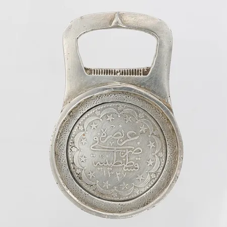 Flasköppnare/kapsylöppnare med myntliknande föremål, höjd 76mm, bredd 49mm, silver 900/1000 Vikt: 83 g