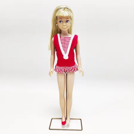 Barbiedocka, #950 Skipper, Straight leg skipper, blond, tillverkad 1964-1966, märkt "Skipper ©1963 Mattel, Inc.", komplett med baddräkt, sandaler (obs! saknar en sandal), hårband, och örhängen, missfärgade örsnibbar, metallstativ, inga övriga tillbehör. Vikt: 0 g