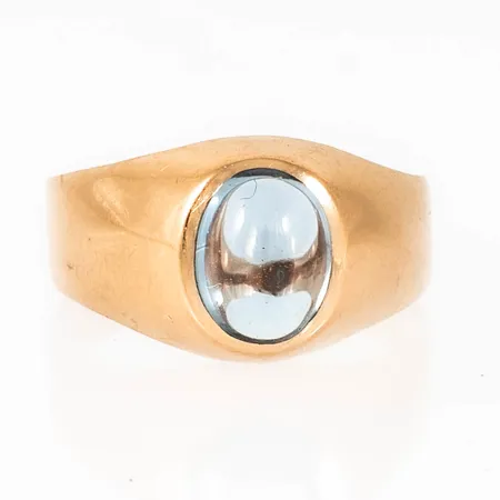 Ring i 18K guld med cabochonslipad ljusblå sten. Den är 3,8 - 11,2 mm bred, är i storlek 19 och väger 3,4g inklusive sten. Tillverkad 1958 av Trege Guldsmedsaktiebolaget i Göteborg. Stämplad 18K & Kattfot.