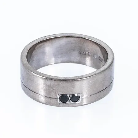 Ring i 18K vitguld med 2 x 0,08ct svarta diamanter. Den är 8,5 mm bred, är i storlek 21 och väger 18,3g. Caratvikt graverad i ringen. Stämplad JPJ (Jannerberg Guldsmide, Göteborg), O11 (2012).