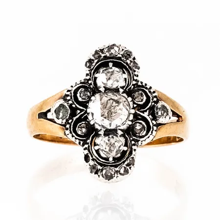 Ring i 18K guld, med 18 rosenslipade diamanter fattade i silver. Den större diamanten i mitten är c:a Ø 4,5 mm och de två på var sida om den c:a Ø 2,5 mm. De mindre diamanterna är c:a Ø 1 - 1,5 mm. Den är 2,7 - 15,5 mm bred, är i storlek 17 och väger 4,0g. Stämplad CGH (CG Hallberg, Uppsala, 18K & Kattfot. Otydlig årsstämpel K8 ? (1936 ?) Sten saknas. Ett par skadade stenar. Gravyr.