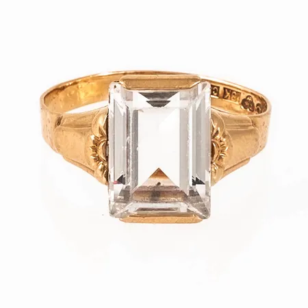 Ring i 18K guld med vit sten. Den är 2,4 - 11,8 mm bred, är i storlek 17 och väger 2,8g inklusive sten. Stämplad C9 (1953), K&EC (Ceson Guldvaru AB, Göteborg), 18K & Kattfot.Naggade facetter på sten. Ojämn skena. 