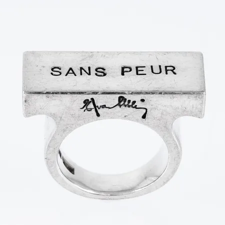 Statement - ring i silver (925/1000) med "Sans Peur" - "utan rädsla" som stansat budskap. Den är 5,3 - 11,3 mm bred, ovandel 11,3 x 28,4 mm, är i storlek 17 och väger 26,8g. Design: Efva Attling. Originalask medföljer. Nypris 5400:- Repor.