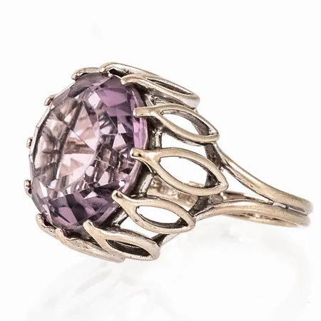 Ring i 18K vitguld med stor ljuslila sten. Den är 2,5 - 17,8 mm bred, är i storlek 17½ och väger 7,9g inklusive sten. Tillverkad 1973 av Heribert Engelbert AB, Stockholm. Naggade fasetter. 