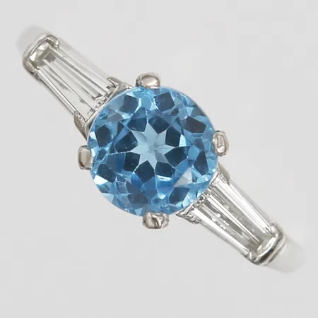 Ring med blå topas ca 1,75ctm samt trapetsslipade diamanter 2 x ca 0,10ct, kvalitet ca Cr-TCa(J-K)/VS-SI, stl: 17½,  platina 900/1000 Vikt: 5,1 g