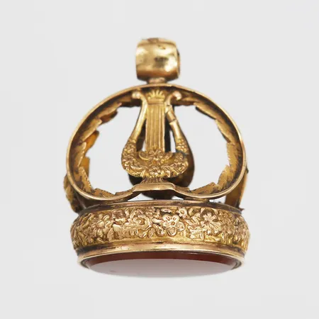 Sigillstamp med karneol, rik dekor av blommor och parställda lyror, 1800-talets andra hälft, slitage, ögla med lagning, dekorbortfall, bucklor, 18K, bruttovikt 10,2g 