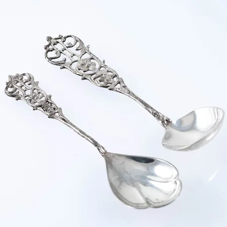 Två kompott/sockerskedar i silver (830/1000), längd 120 och 125 mm. Stämplade GEWE (Gewe Silvervarufabriken AB, Malmö), Silverstämpel & Kattfot. Vikt: 30,0g.