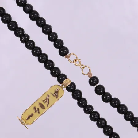 Collier med svarta stenar caØ6mm,  45cm, hänge med hieroglyfer, ca 40,5x9mm inkl ögla, i behov av omträdning. 18K Bruttovikt 246,3g 