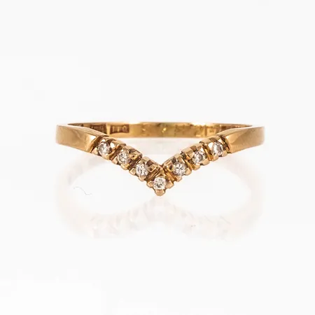 Ring i 18K guld: V-formad med 7 x 0,01ct briljantslipade diamanter. Den är i storlek 16½. Skenans bredd 1,4 - 1,8. Vikt: 1,8g. Stämplad HE (Hans Engelbert, Stockholm) STIGBERT, I10 (1983), 18K & kattfot. Stenstorlek graverad. Gravyr.