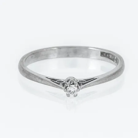 Ring i 18K vitguld med en briljantslipad diamant 0,04ct. Den är i storlek 18. Skenans bredd 1 - 2,2 mm. Vikt: 2,2g. Stenstorlek ingraverad. Stämplad APP, F10 (1980), 18K & Kattfot.