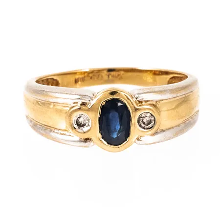 Ring i 18K guld med ovalslipad blå safir c:a 4 x 6 mm och 2 x c:a 0,03ct diamanter. Den är 2,2 - 7,8 mm bred, är i storlek 18¾ och väger 4,4g. 