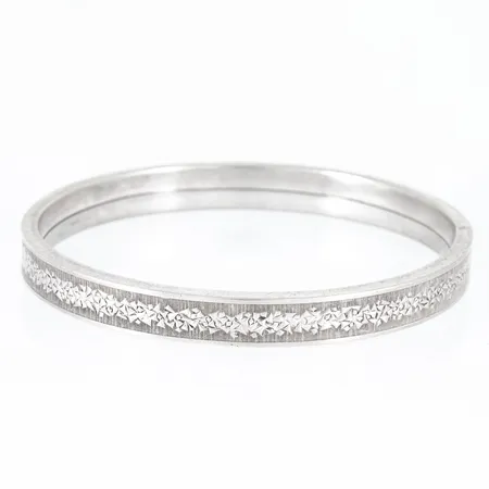 Armring i silver (835/1000) med mönsterdekor. Öppningsbar (ej gångjärn), innermått 63 x 55 mm, 8 mm bred och väger 16,2g. Silverstämpel & Svensk importstämpel.