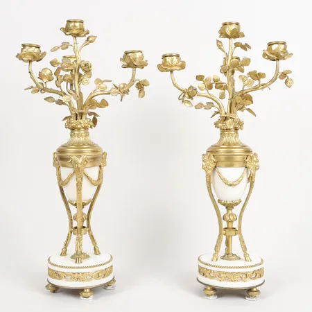 Ett par Kandelabrar för fyra ljus vardera, Louis XVI-stil, 1800-talets andra hälft, förgylld brons och marmor, dekor av bockhuvuden, höjd: ca 43cm, åldersbetingat slitage, något sneda, mindre dekorbortfall. Specialfrakt, kontakta pantbankskontoret för mer information.