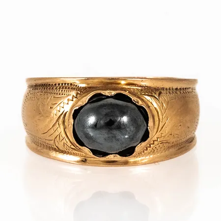Doserad ring i 18K guld med hematit. Den är i storlek 20, är 5,2 - 10,8 mm bred och väger 4,3g. Stämplad G9 (1957), JBB (Dahlströms Guldsmedsaffär, Arboga), 18K & Kattfot. Sten lös. Gravyr.