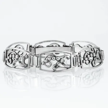 Armband i silver, mönsterdekor blommor. Det är 18,5 cm långt, är 6,5 - 16,2 mm brett och väger 24,0g. Silver & Svensk importstämpel. 