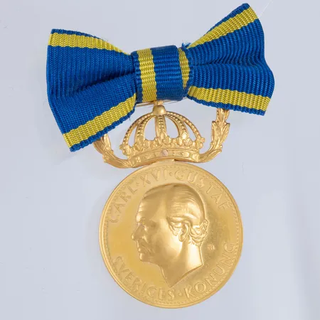 Förtjänstmedalj i 23K guld med bandfäste i 18K guld. C:a 10g 23K & 4,0g 18K. Namngravyr.