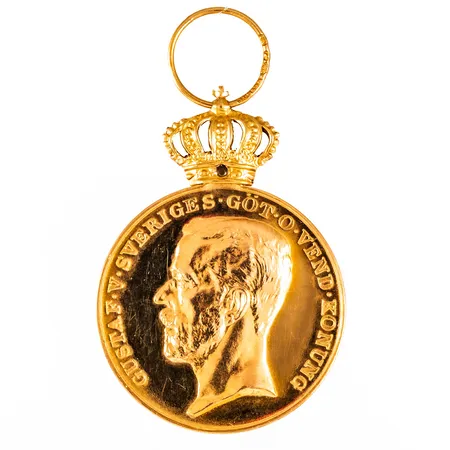 Förtjänstmedalj i 23K guld med bandfäste/krona i 18K guld. Ø 31,3 mm. Namngravyr. Totalt 20,9g.