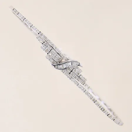 Armband med briljantslipade diamanter ca 80 x 0,01ct samt baguetteslipade 10 x ca 0,01ct, flertalet diamanter indikerar på att vara syntetiska, längd 17,5cm, bredd 1,5-8mm, vitguld, ojämnheter, något trögt lås, 18K  Vikt: 7,5 g
