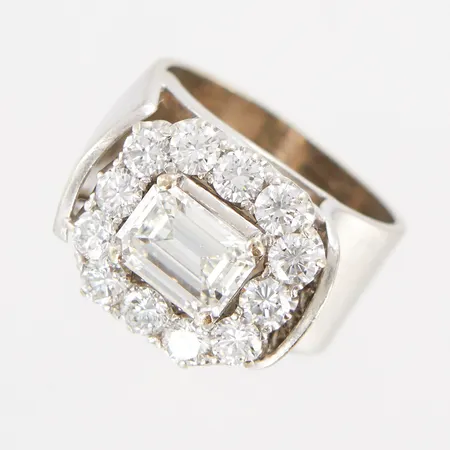 Ring med en smaragdslipad diamant ca 1,30ct I-J/VS1 samt briljantslipade diamanter ca 9x0,10ct G-H/SI1, av Elon Arenhill år 1985, stl 15¾, mått framtill ca 13x16mm, några micronagg på mittsten, 18K Vikt: 12,5 g