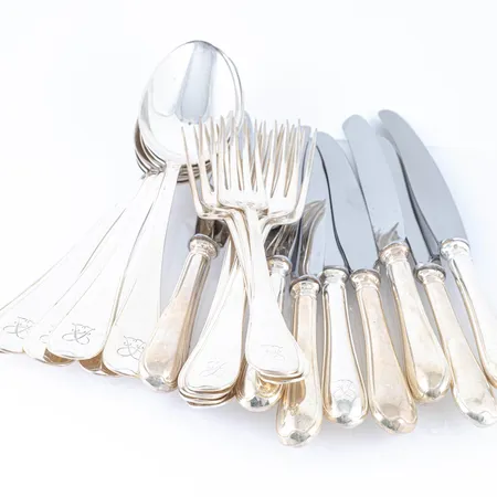 Svensk i silver (830/1000): åtta bordsgafflar (18 cm), sex bordsskedar (20,5 cm) & åtta knivar med rostfria blad (två stycken 20,5 cm, sex är 22 cm). Gafflar & skedar väger 603g tillsammans. Knivarna väger 370g bto. Samtliga med monogramgravyr. 