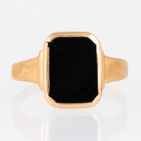 Klackring i 18K guld med svart sten (onyx el. agat). Den är i storlek 19¾, är 2,2 - 14 mm bred och väger 3,9g. Stämplad R8, GVH, 18K & kattfot. Vass och nött fattning. Repig sten.