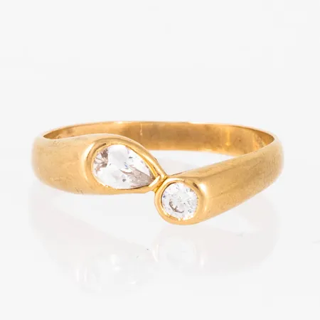 Ring i 18K guld med två vita stenar. Den är i storlek 21¼, är 2,9 - 5,7 mm bred och väger 4,3g. Stämplad SGP, 750. Naggade facetter på en sten.