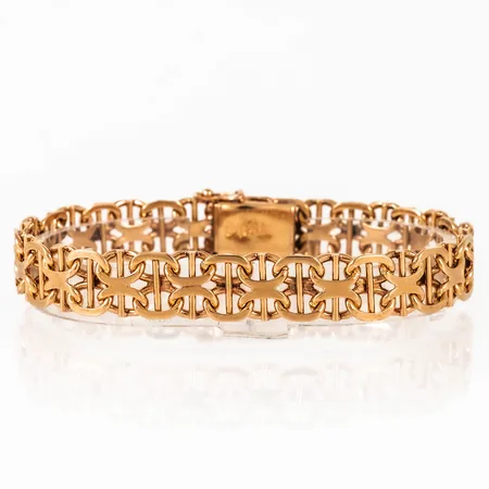 Armband, X-länk med stav i 18K guld. Det är 19,5 cm långt, är 10,2 mm brett och väger 29,0g. Kistlås. Stämplad T9 (1969), SGT (Svenska Guldvaruaktiebolaget, Stockholm), 18K & Kattfot.