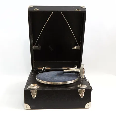 Vevgrammofon 1900-talets första hälft, bruks- samt åldersrelaterat slitage, defekt fäste till ljuddosan/pickupen annars i fungerande skick, tillhörande vev samt 21 stenkakor medföljer  Specialfrakt, kontakta pantbankskontoret för mer information.