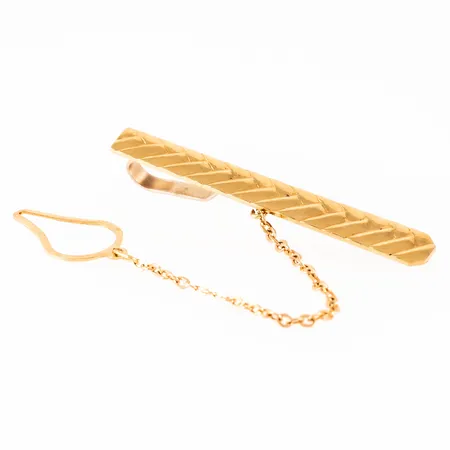 Slipsklämma i 18K guld. Den är 5,2 - 6,1 mm bred,  50,2 mm lång och väger 6,3g. Säkerhetskedja. Stämplad 750.