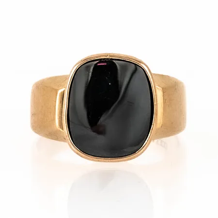Klackring i 18K guld med hematit. Den är i storlek 19¾, är 4 - 14,8 mm bred och väger 6,7g. Tillverkad 1963 av Ceson i Göteborg. Stämplad 18K & kattfot. 