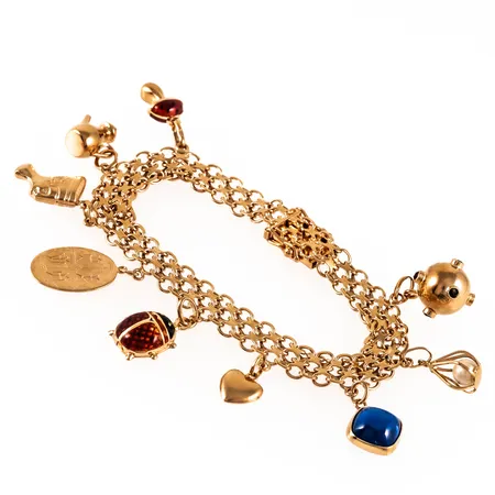 Armband X-länk i 18K guld med nio berlocker: Trolltrumma, tekanna, nycklepiga. Det är 19,3 cm långt, 8,5 mm brett och väger 26,4g. Kistlås. Stämplad N9, ÄSA, 18K & kattfot. En defekt berlock. 