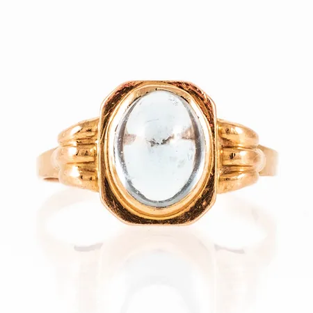 Ring i 18K guld med ljusblå cabochonslipad sten. Den är i storlek 18, är 1,3 - 11 mm bred och väger 2,6g. Stämplad E9 (1955), K&EC, 18K & kattfot. Repor på sten, men fin lyster ändå.