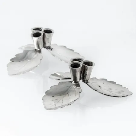 Ett par ljusstakar i vitmetall med björklövsdekor. Vardera rymmer tre Ø 8 mm ljus, alternativt doftpinnar. De är Ø 8 cm i botten.  Vikt: 0 g