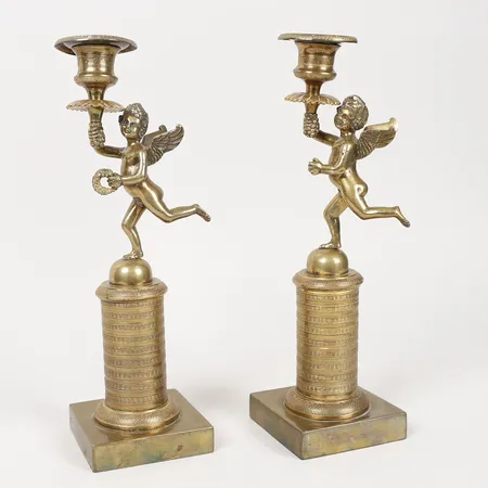 Ett par ljusstakar, Empire, 1800-tal, troligen Ryssland, mässing, dekor av Putti bärandes fackla samt krans på postament, krans saknas, sprickor, lagningar, åldersbetingat slitage.  Skickas med postpaket.