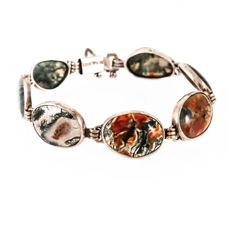 Armband i silver med mossagat. Det är 20,5 cm långt, är 13,5 - 18 mm brett och väger 25,7g. Kistlås med säkerhetskedja. Tillverkat 1961 av Victor Janson Guldvaru AB, Lindesberg. Stämplad silver & kattfot.