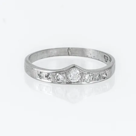 Doserad alliansring i 18K vitguld med sju diamanter ca 0,01 - 0,12 ct briljant- och åttkantslipade, totalt 0,23ct. Den är i storlek 18, är 2 - 4,3 mm bred och väger 2,3g. Stämplad V9 (1971), ALTON, 18K & kattfot. Mittsten nedslipad kulett som sticker ut invändigt.