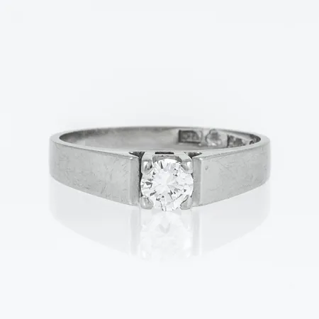Ring i 18K vitguld med en briljantslipad diamant 0,26ct i fyrklofattning. Den är i storlek 16½, är 2 - 4 mm bred och väger 3,3g. Stenstorlek 0,26 ingraverad. Stämplad R9, JP, 18K & kattfot.