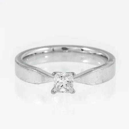 Ring i 18K vitguld med 1 x 0,30ct (c:a W/vs) prinsesslipad diamant i fyrklofattning. Den är i storlek 17, är 3,5 mm bred och väger 5,5g. Stämplad SCH (Schalins Ringar, Östersund), 18K & kattfot. Stenstorlek 0,30ct ingraverad.