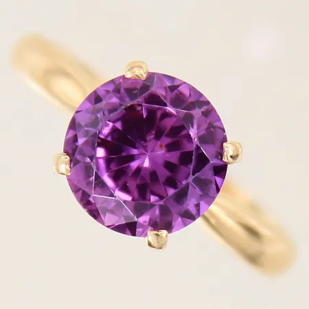 Ring med lila syntetisk korund, stl 19¾, bredd 3-10mm, sten med nagg, gravyr, 18K  Vikt: 5,2 g